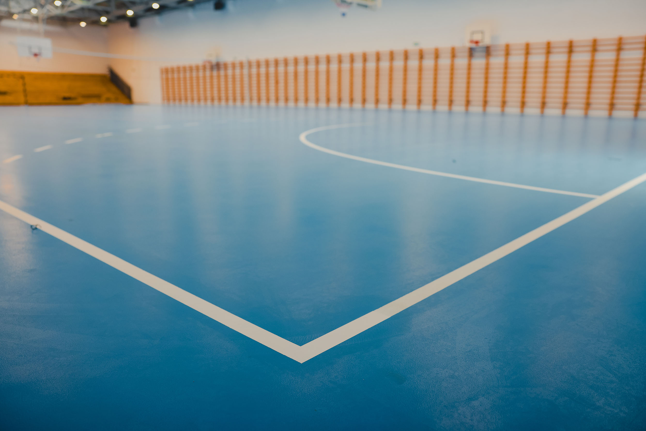 Indoor sports hall with blue epoxy floor and white lines defining playing area for sports activities